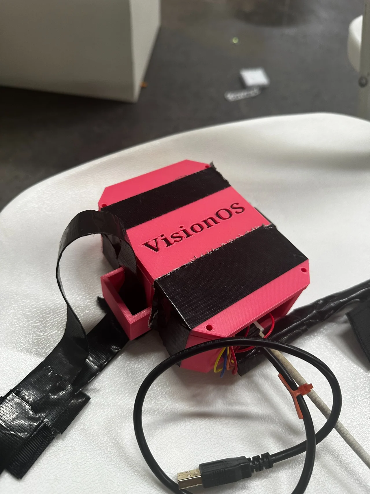 Close-up of the pink VisionOS enclosure with the VisionOS name, black straps, and connected wiring.